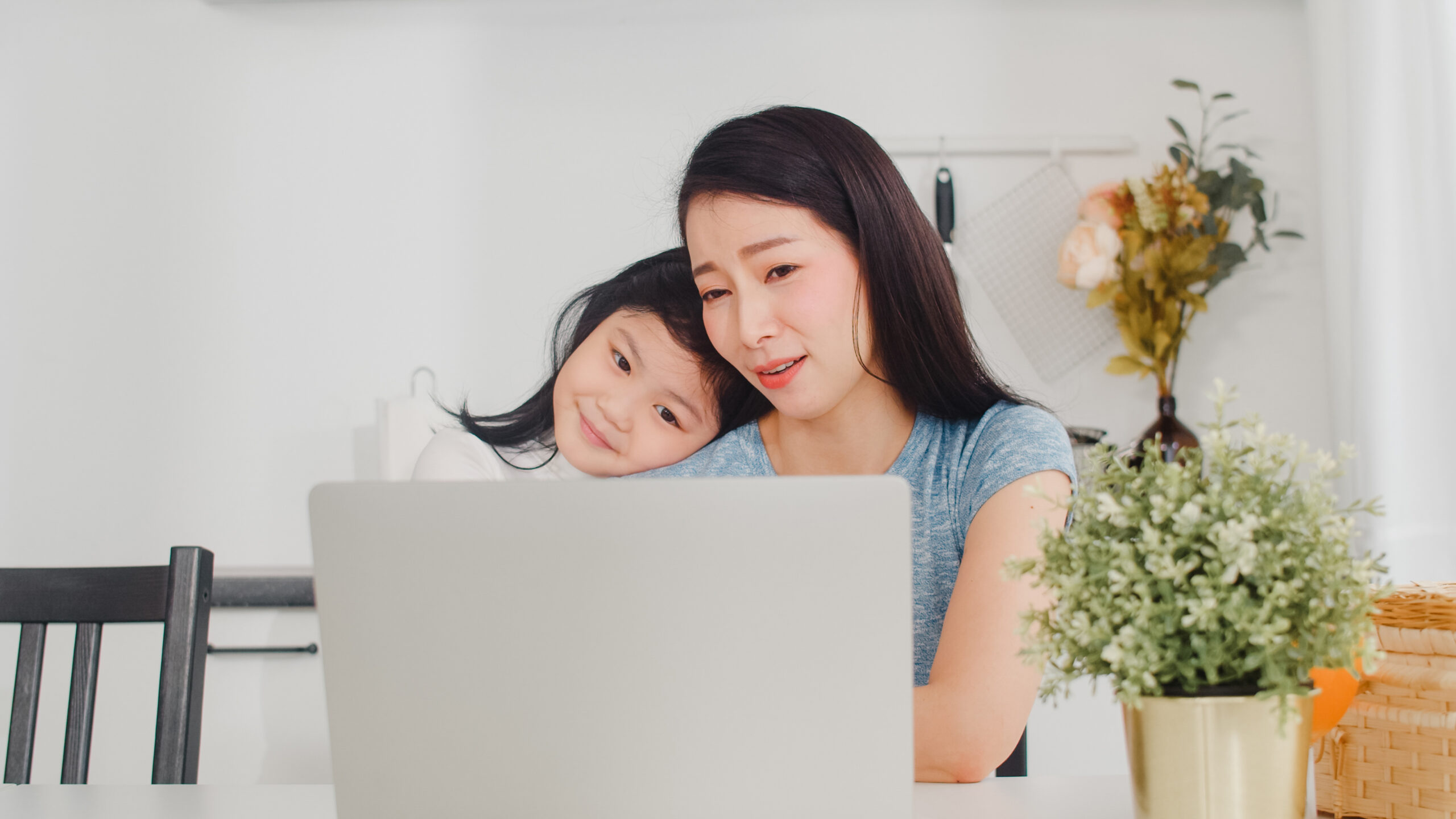 Young Asian businesswoman serious, stress, tired and sick while working on laptop at home. Young daughter consoling her mother who working hard in modern kitchen at house in the morning concept.